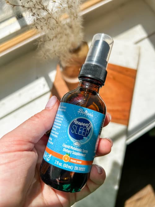 Hand holding a bottle labeled Bolton's Naturals Heavenly Sleep with a blue label against a neutral background.